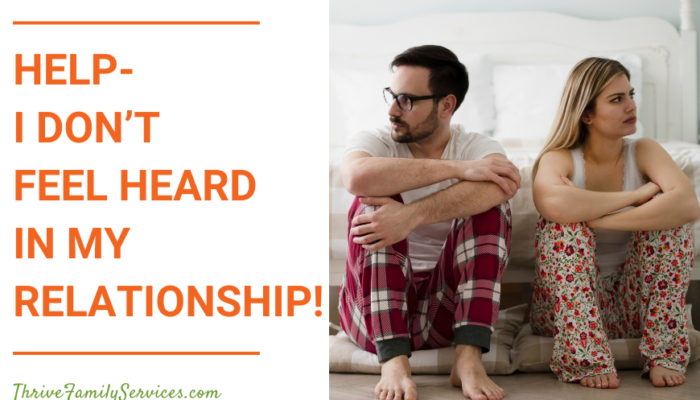 orange text that reads "Help-I Don't Feel Heard in My Relationship!" next to a photo of a man and a woman in pajamas, sitting on the floor at the foot of a bed. their arms are crossed and they are looking away from one another. they are visibly tense. | Denver Colorado Relationship Therapy