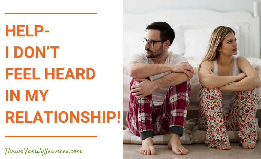 orange text that reads "Help-I Don't Feel Heard in My Relationship!" next to a photo of a man and a woman in pajamas, sitting on the floor at the foot of a bed. their arms are crossed and they are looking away from one another. they are visibly tense. | Denver Colorado Relationship Therapy