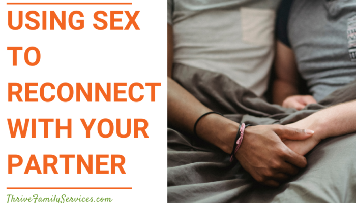 Orange text over a white background "Using Sex to Reconnect With Your Partner" to the left of a photo of an interracial couple in sitting next to each other, holding hands on a set of gray sheets. We can only see from their chests down to their laps. | Aurora Colorado Sex Therapist Couples Counseling
