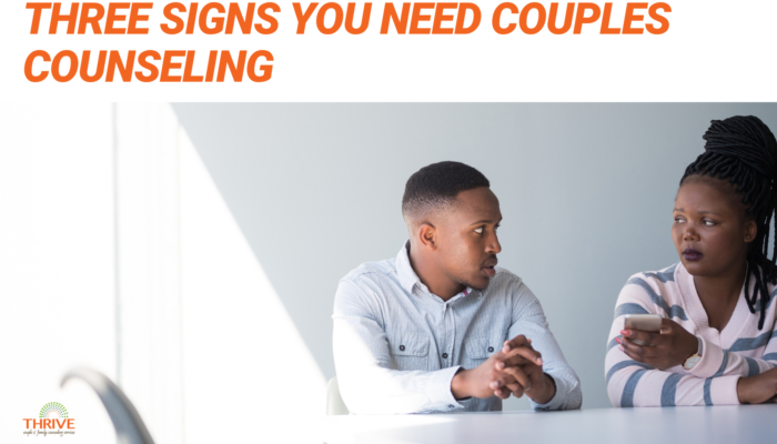 orange text that reads "3 Signs You Need Couples Counseling" above a photo of a man and a woman of color seated at a white counter. she has her arms crossed and he is holding his hands on the table. They look upset.