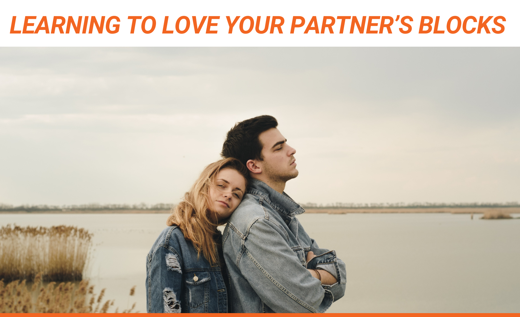 Orange text that reads "Learning to Love Your Partner’s Blocks" above a stock photo of a white heterosexual couple standing on the edge of a body of water. Both are wearing denim jackets. The woman is behind the man, leaning on his back, and he's facing away from her.
