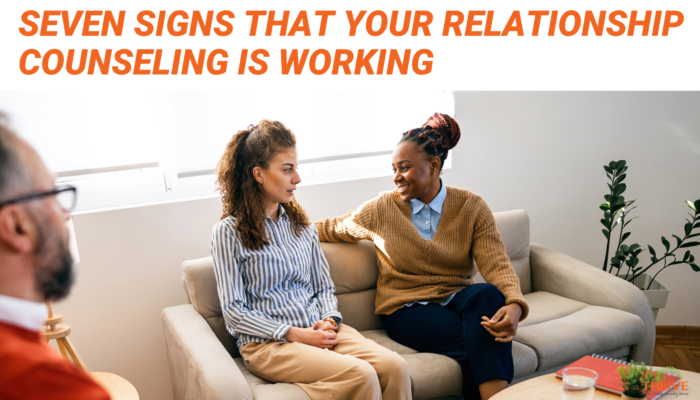 Dark orange text that reads "Seven Signs That Your Relationship Counseling is Working" above a stock photo of an interracial lesbian couple sitting on a couch in a counseling office, with their counselor, a man, in the bottom left corner.